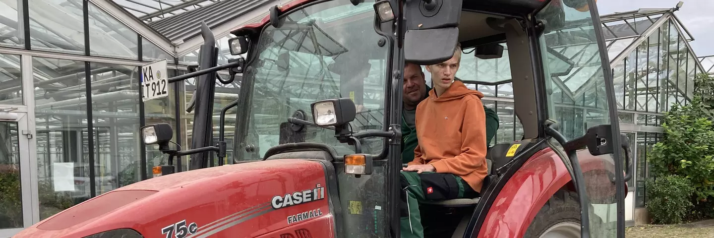 Ein Mitarbeiter der Terra Medica zusammen mit einem Jugendlichen mit Behinderung auf einem Traktor auf der Terra Medica