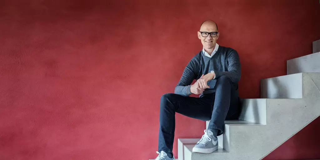 Dr. Traugott Ullrich sitzend auf einer Treppe vor einem roten Hintergund